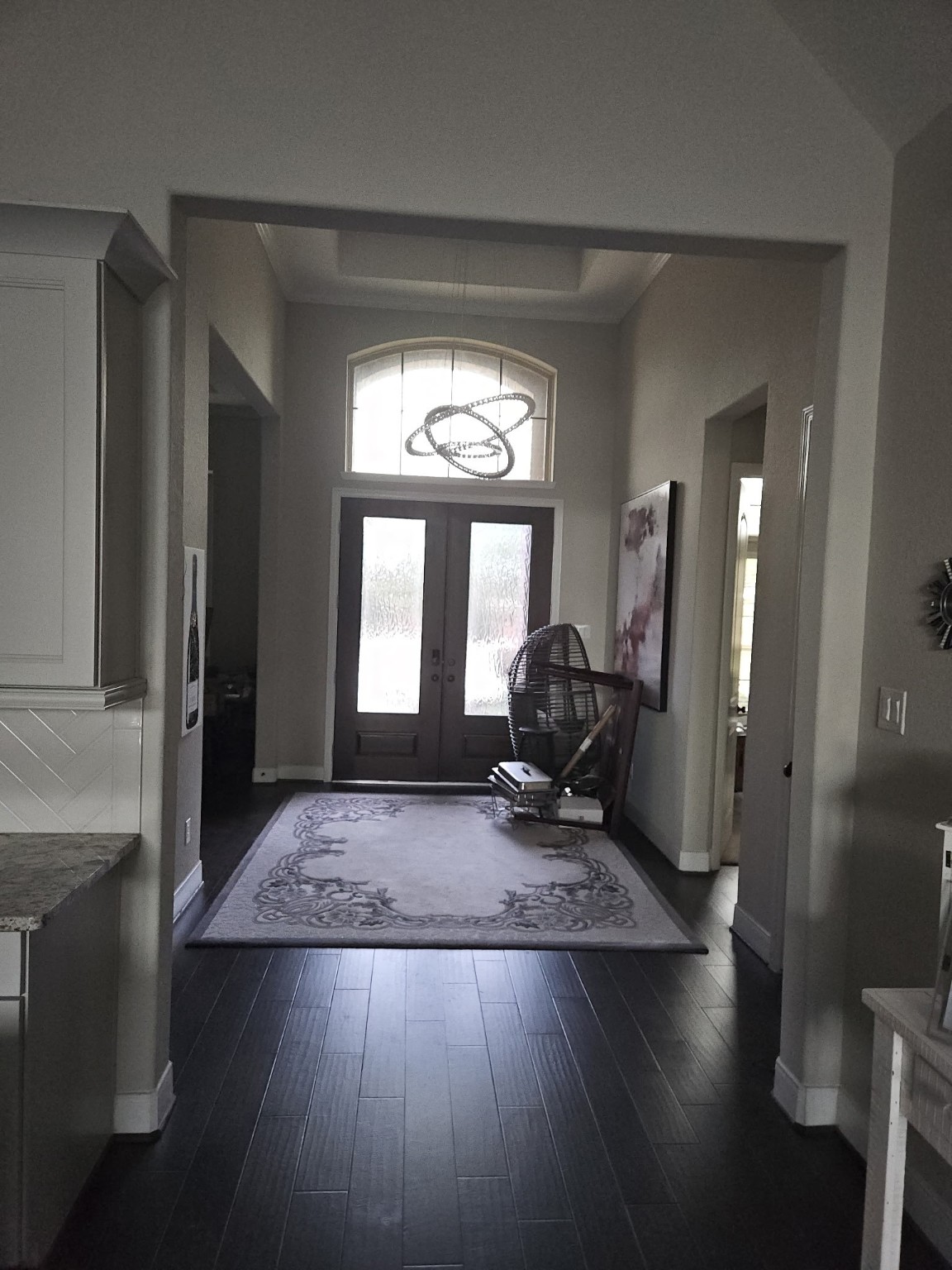 18919 Steep Step Trail Cypress, TX 77433 - Photo 7 of 12 This entryway features high ceilings and dark hardwood floors, creating an elegant and welcoming atmosphere. A large rug and wall art enhance the space, while double doors with frosted glass allow natural light to illuminate the area.