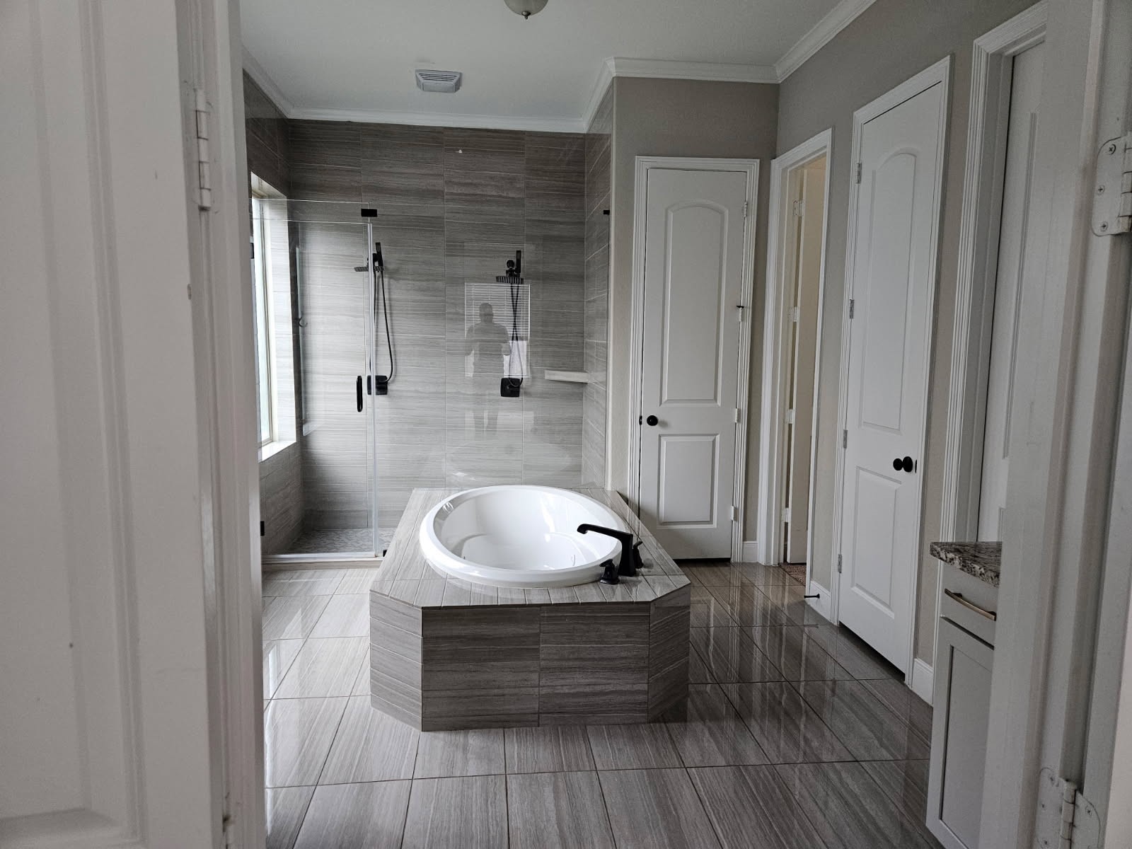 18919 Steep Step Trail Cypress, TX 77433 - Photo 9 of 12 This bathroom features a modern design with a central, built-in bathtub and a glass-enclosed shower. The neutral color scheme and sleek tile flooring create a clean, spacious feel. Ample storage is provided by multiple doors and cabinets.