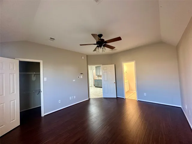 a view of an empty room with wooden floor and a ceiling fan