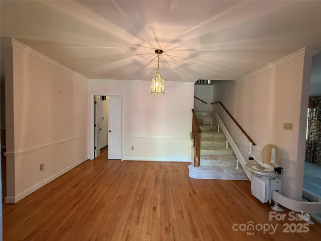 a view of an empty room with wooden floor stairs and a chandelier