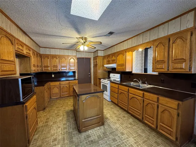 a large white kitchen with stainless steel appliances granite countertop a stove a sink dishwasher and cabinets with wooden floor