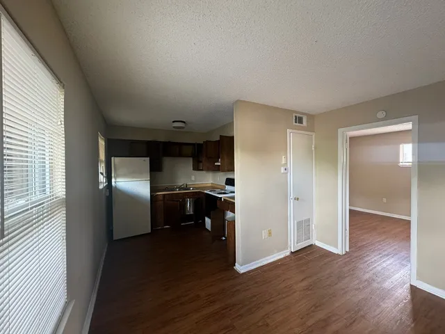 a view of empty room with wooden floor and kitchen view