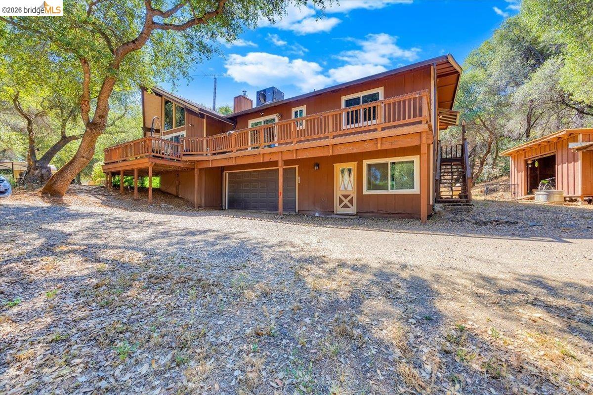 8733 Fraguero Road Sonora, CA 95370 - Photo 7 of 73 Two-story residence featuring a wood-sided exterior, a full-width upper deck with wood railing, an attached garage, an exterior wooden staircase, and a separate outbuilding