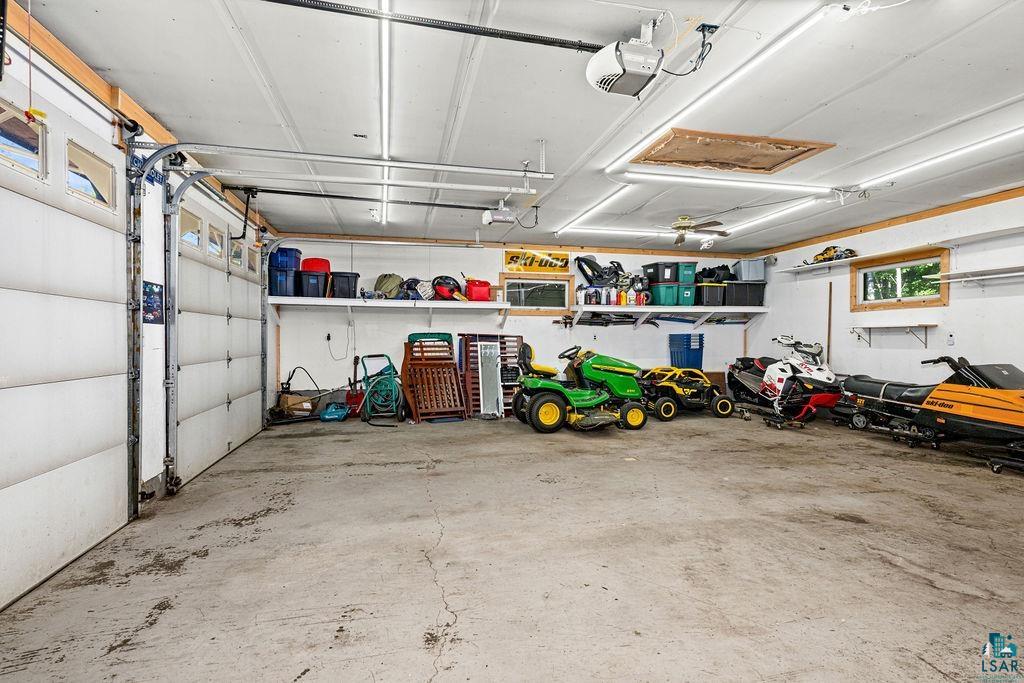 5370 Ugstad Road Hermantown, MN 55811 - Photo 7 of 68 Expansive garage space with concrete flooring, multiple overhead fluorescent light fixtures, two garage door openers, built-in shelving, and transom windows