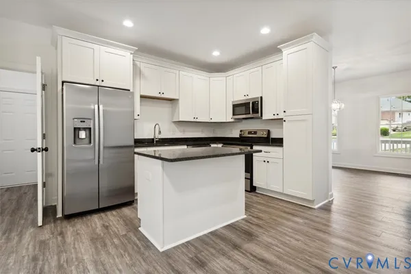 a kitchen with stainless steel appliances granite countertop a refrigerator a stove a sink and white cabinets with wooden floor