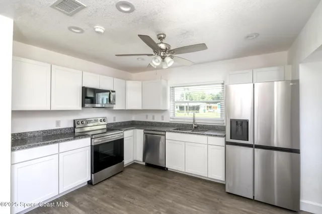 a kitchen with stainless steel appliances granite countertop white cabinets a sink a window a refrigerator and white cabinets