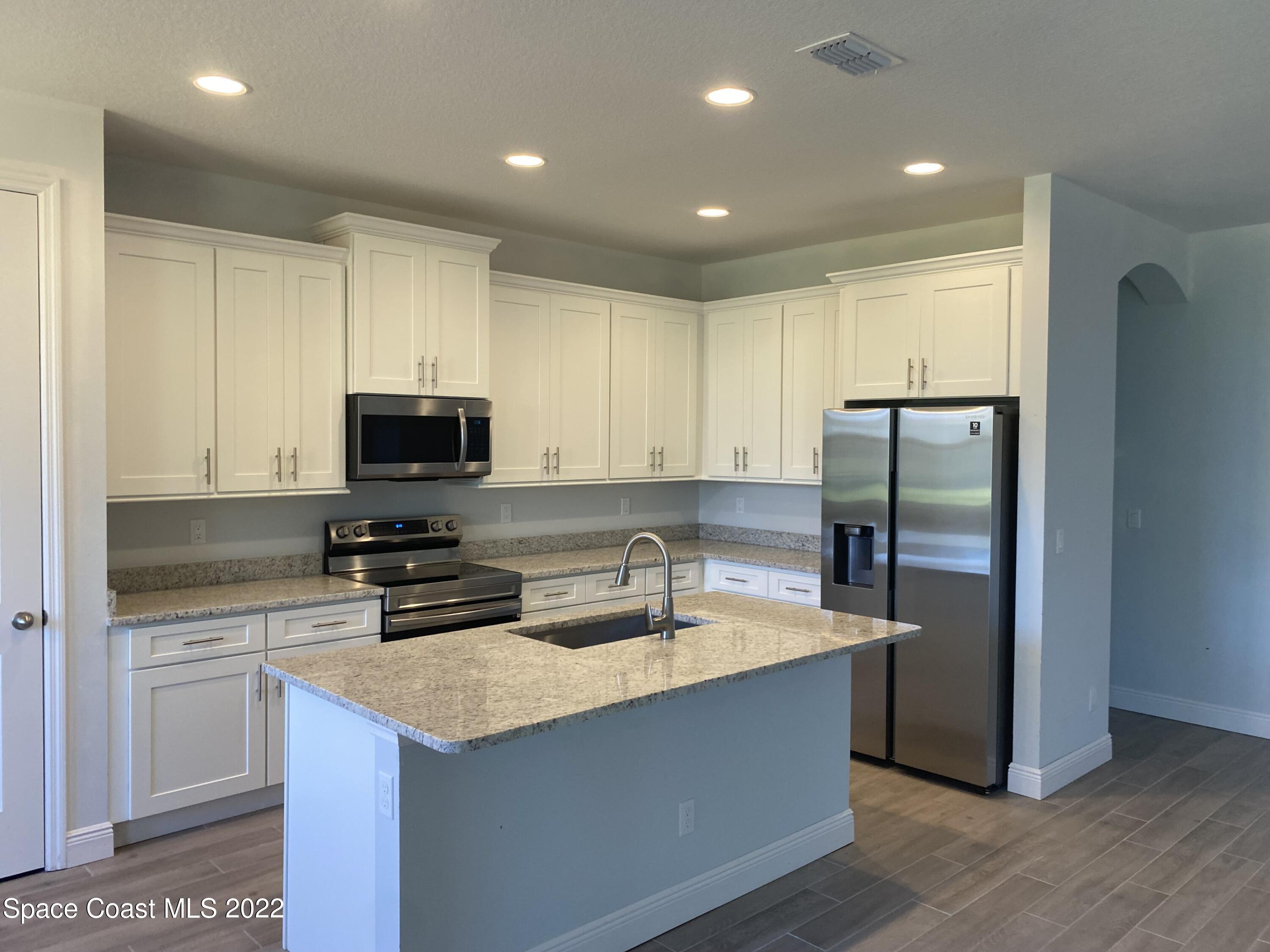 1376 Wing Road Southwest Palm Bay, FL 32908 - Photo 9 of 17 a kitchen with stainless steel appliances granite countertop a refrigerator a sink a stove a microwave and island