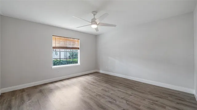 an empty room with wooden floor fan and windows