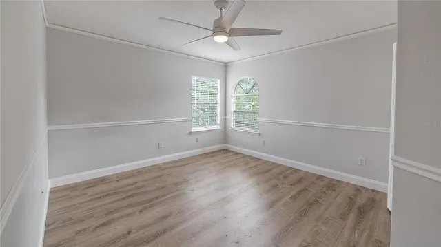 an empty room with wooden floor fan and windows