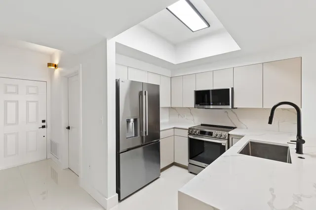 a kitchen with stainless steel appliances kitchen island a refrigerator sink and white cabinets