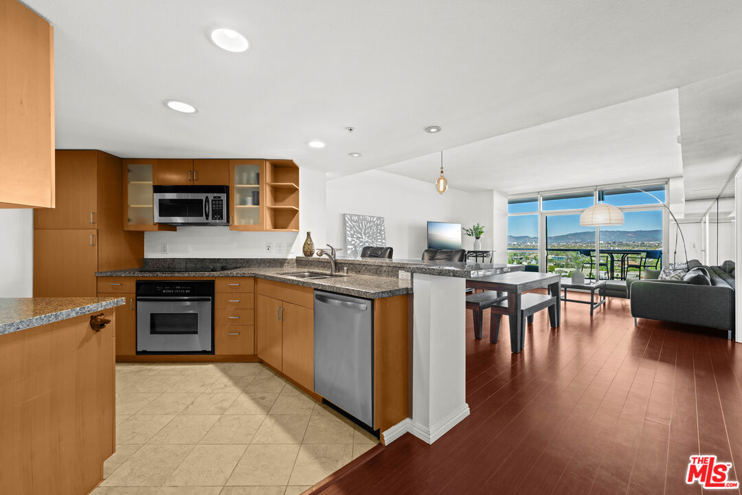 13700 Marina Pointe Drive, Unit 1007 Marina del Rey, CA 90292 - Photo 10 of 53 a kitchen with stainless steel appliances granite countertop a stove top oven a sink a dining table and chairs with wooden floor