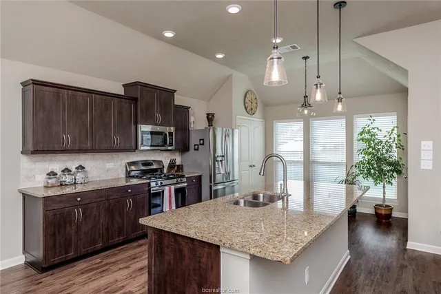 a kitchen with stainless steel appliances granite countertop wooden cabinets a stove a sink and a refrigerator