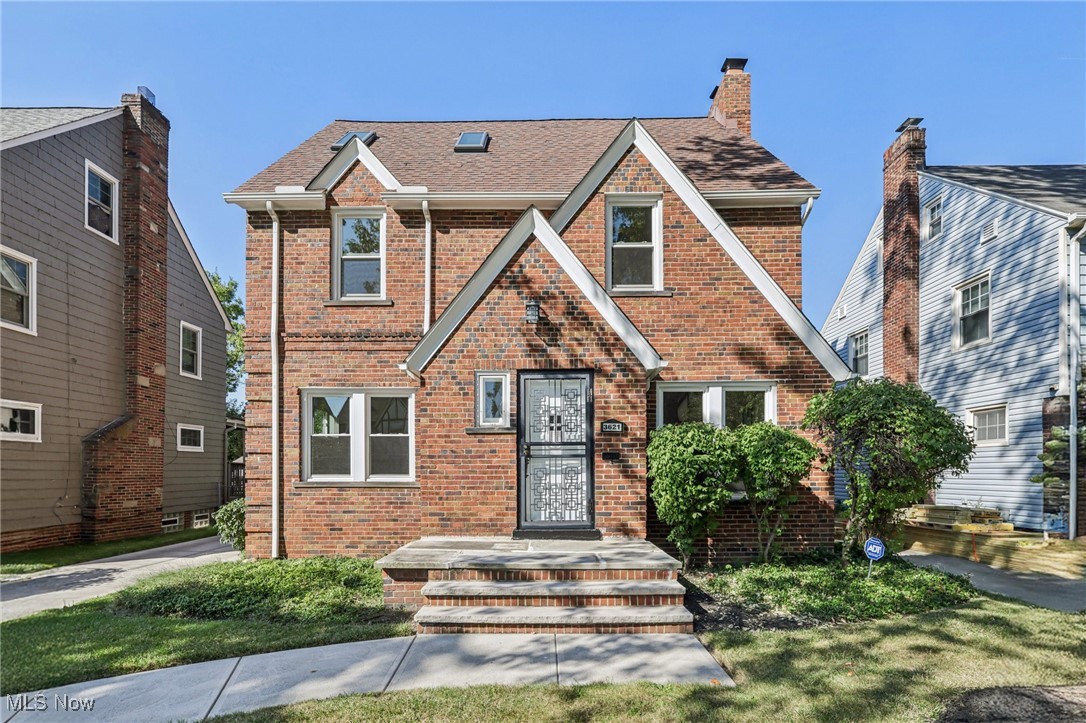 Tudor house with brick siding, a chimney, and roof with shingles