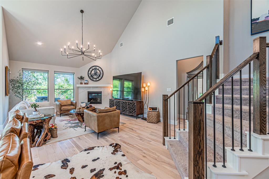 1070 Adair Road Prosper, TX 75078 - Photo 11 of 40 Vaulted living area featuring light wood-finish flooring, a fireplace with a stone surround, and an elegant chandelier