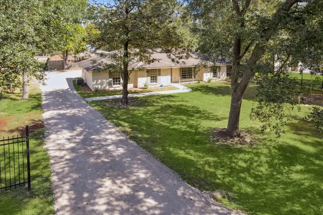 a view of house in front of a big yard with large trees