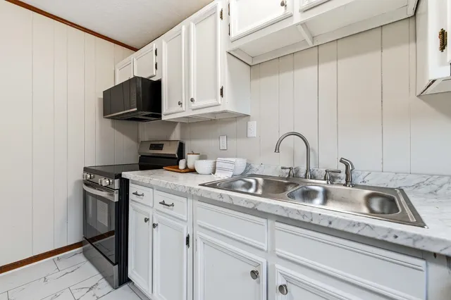 a kitchen with stainless steel appliances granite countertop a sink a stove and a microwave oven with white cabinets
