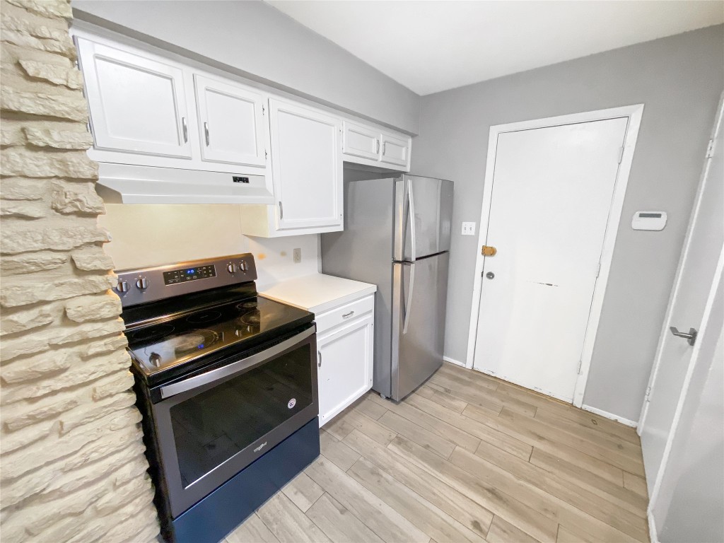 1503 Roundup Trail Round Rock, TX 78681 - Photo 9 of 23 Kitchen featuring stainless steel appliances, white cabinetry, light countertops, under cabinet range hood, and light wood-type flooring