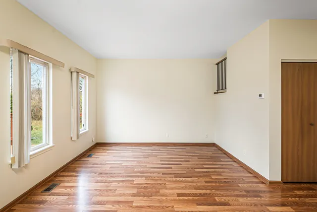 a view of an empty room with wooden floor and a window