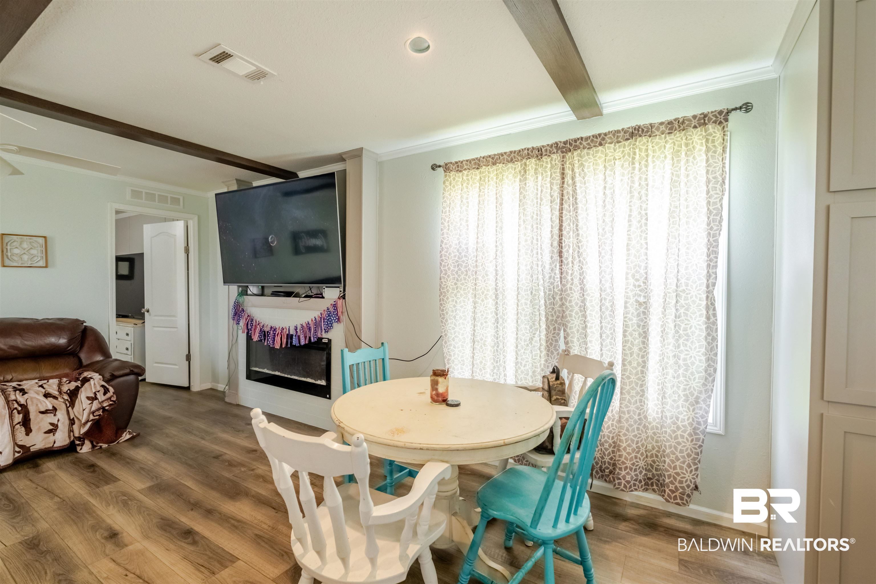 15575 Mikkelsen Road Summerdale, AL 36580 - Photo 13 of 68 Dining area featuring wood-finish flooring, a wall-mounted television above a built-in fireplace, crown molding, and decorative ceiling beams