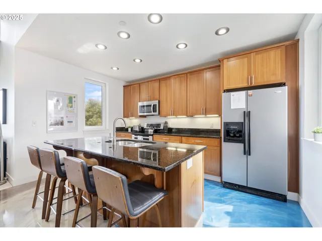 a kitchen with stainless steel appliances granite countertop a refrigerator a sink dishwasher a dining table and chairs with wooden floor