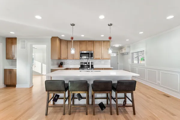 a kitchen with kitchen island granite countertop a dining table chairs refrigerator and cabinets