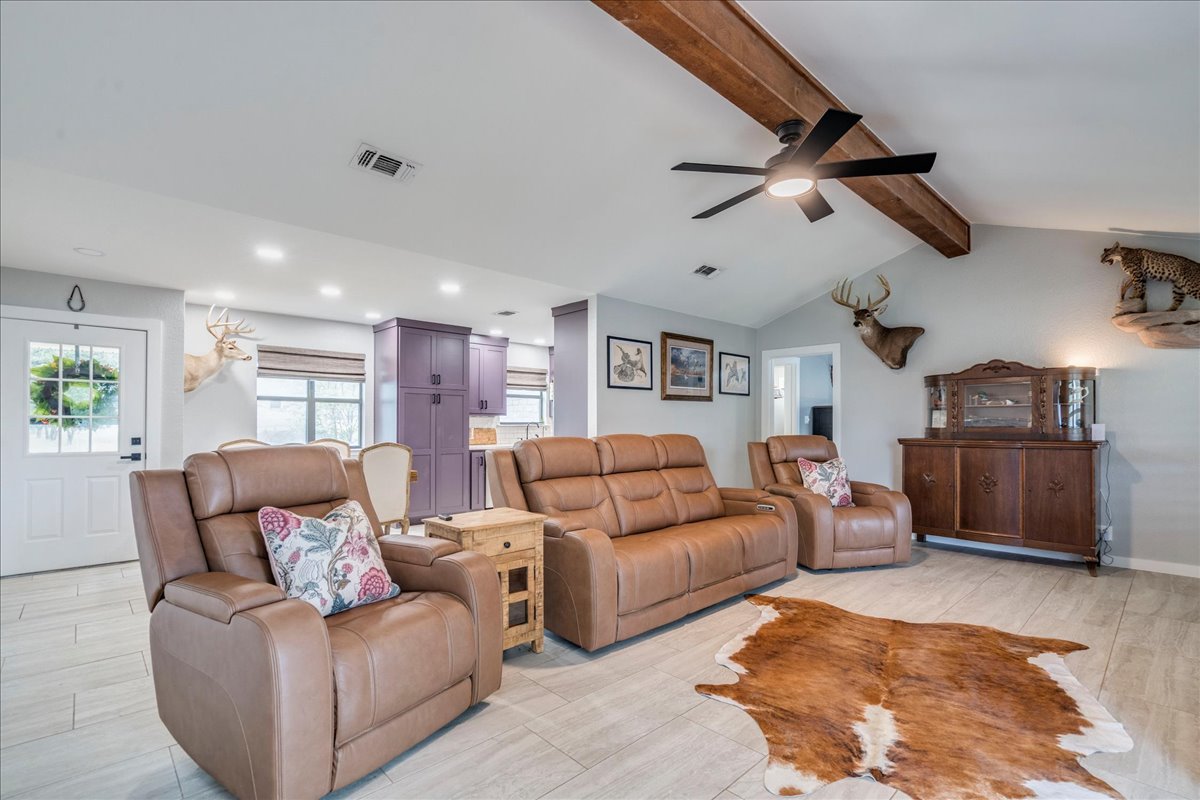 104 Clear Springs Road Georgetown, TX 78628 - Photo 10 of 30 A well-lit great room features vaulted ceilings, exposed wooden beams, and a modern ceiling fan, seamlessly connecting to an open-concept kitchen.
