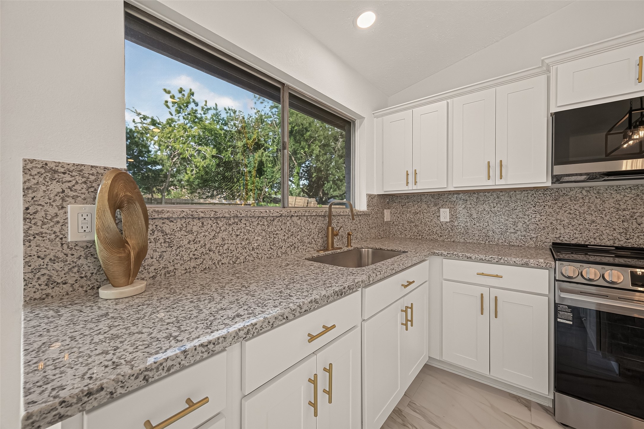 16619 Tibet Road Friendswood, TX 77546 - Photo 10 of 29 This modern kitchen features sleek granite countertops, white cabinetry with gold hardware, a stainless steel sink, and a large window offering plenty of natural light.