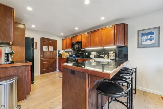 a kitchen with stainless steel appliances granite countertop a refrigerator a sink dishwasher a stove and a dining table with wooden cabinet