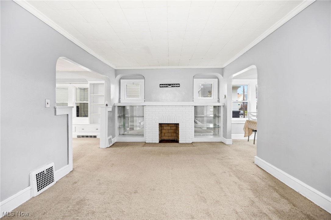3368 Berea Road Cleveland, OH 44111 - Photo 3 of 26 Unfurnished living room featuring arched walkways, carpet, ornamental molding, and a brick fireplace
