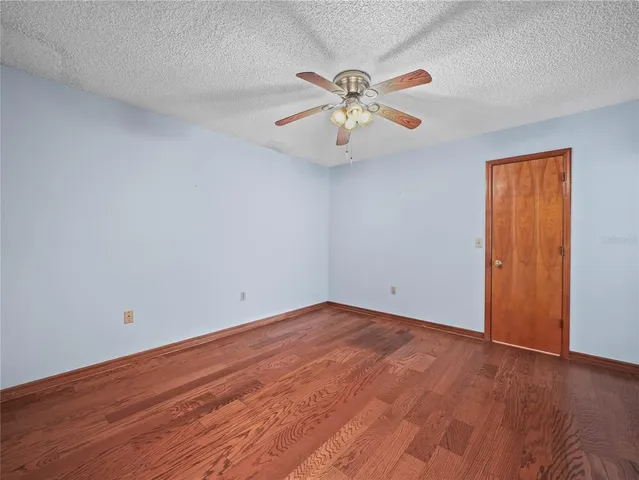 a view of an empty room with wooden floor and a ceiling fan