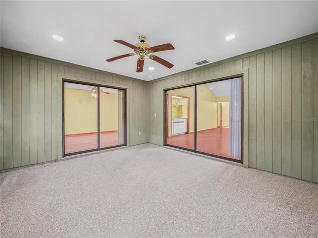 an empty room with chandelier fan and windows