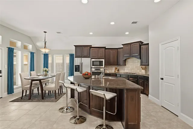 a kitchen with stainless steel appliances granite countertop a stove top oven a sink a dining table and chairs
