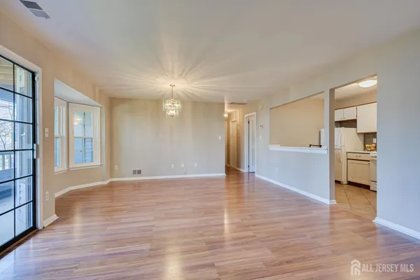 a view of an empty room with wooden floor and a kitchen