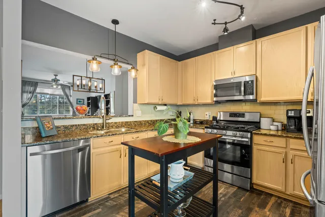 a kitchen with stainless steel appliances granite countertop a stove top oven a sink dishwasher and white cabinets with wooden floor