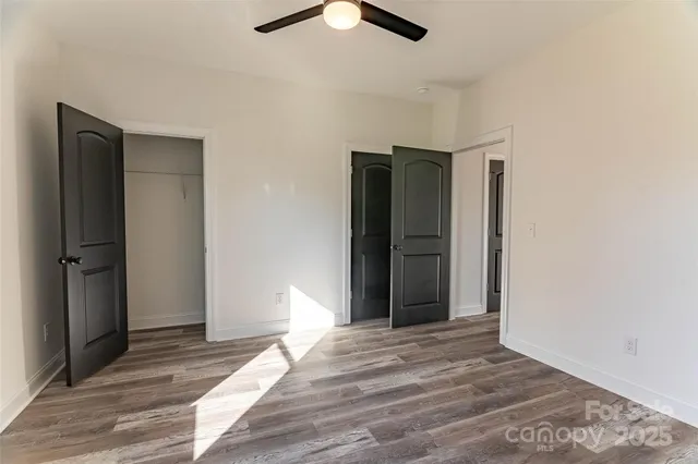 a view of an empty room with wooden floor and a ceiling fan