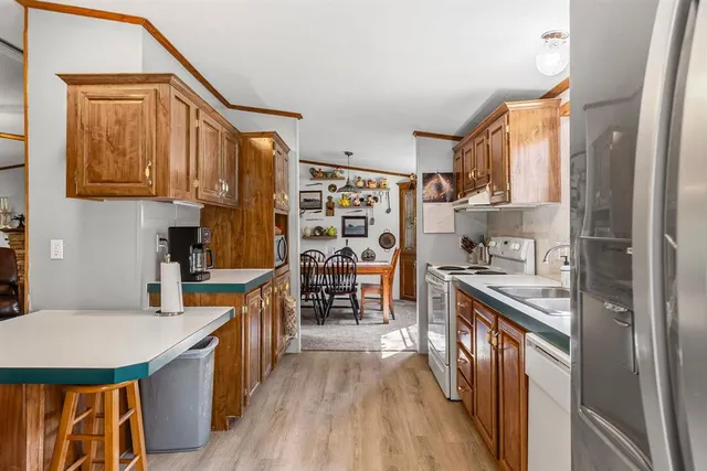 a kitchen with stainless steel appliances granite countertop a stove top oven a sink a refrigerator and white cabinets with wooden floor