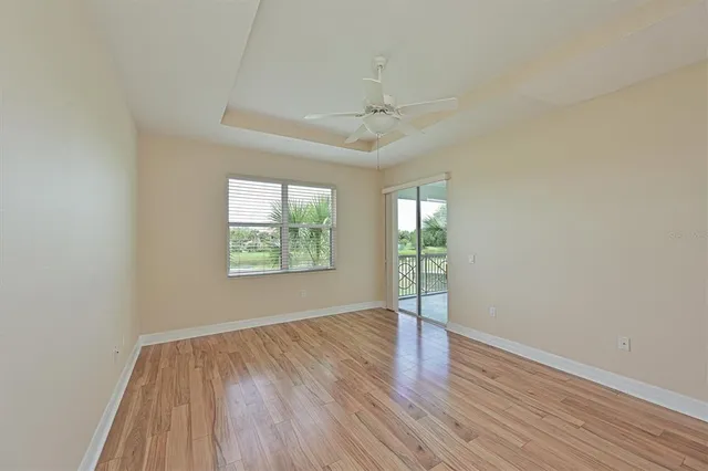 an empty room with wooden floor chandelier fan and windows