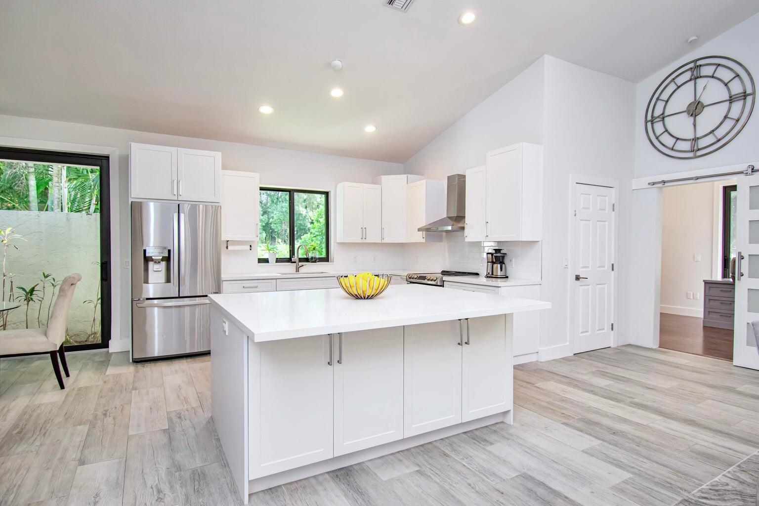 2302 Northwest 66th Drive Boca Raton, FL 33496 - Photo 18 of 53 a kitchen with stainless steel appliances a refrigerator a sink a stove and white cabinets with wooden floor