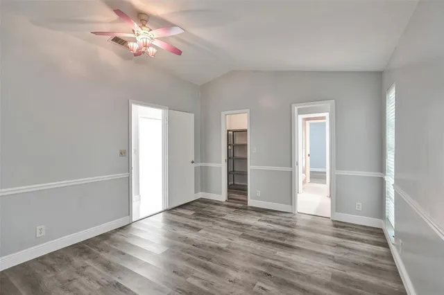 an empty room with wooden floor chandelier fan and windows