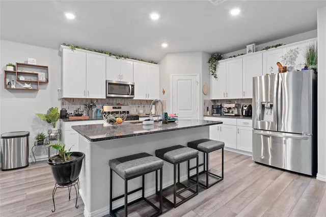 a kitchen with stainless steel appliances a stove a sink a microwave a refrigerator and white cabinets with wooden floor