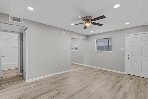 a view of an empty room with wooden floor and a ceiling fan