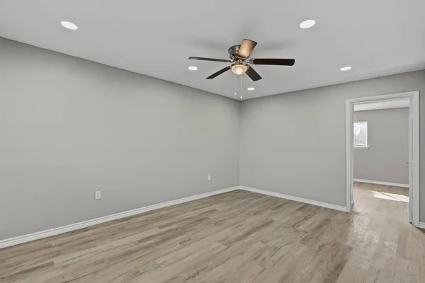 an empty room with wooden floor fan and windows