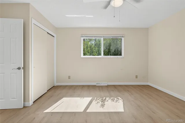 an empty room with wooden floor chandelier fan and windows
