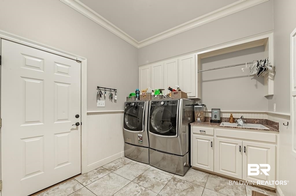 30014 Dolive Ridge Daphne, AL 36527 - Photo 26 of 57 Laundry room with washing machine and clothes dryer, light tile floors, sink, ornamental molding, and cabinets