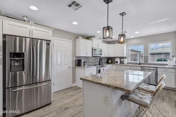 a kitchen with stainless steel appliances granite countertop a refrigerator a sink dishwasher a stove and white cabinets with wooden floor