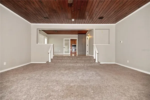 an empty room with wooden floor chandelier and windows