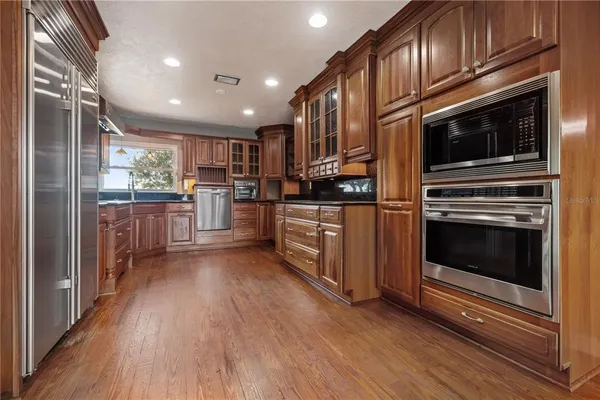 a kitchen with stainless steel appliances granite countertop a refrigerator a sink dishwasher a stove and white countertops with wooden floor