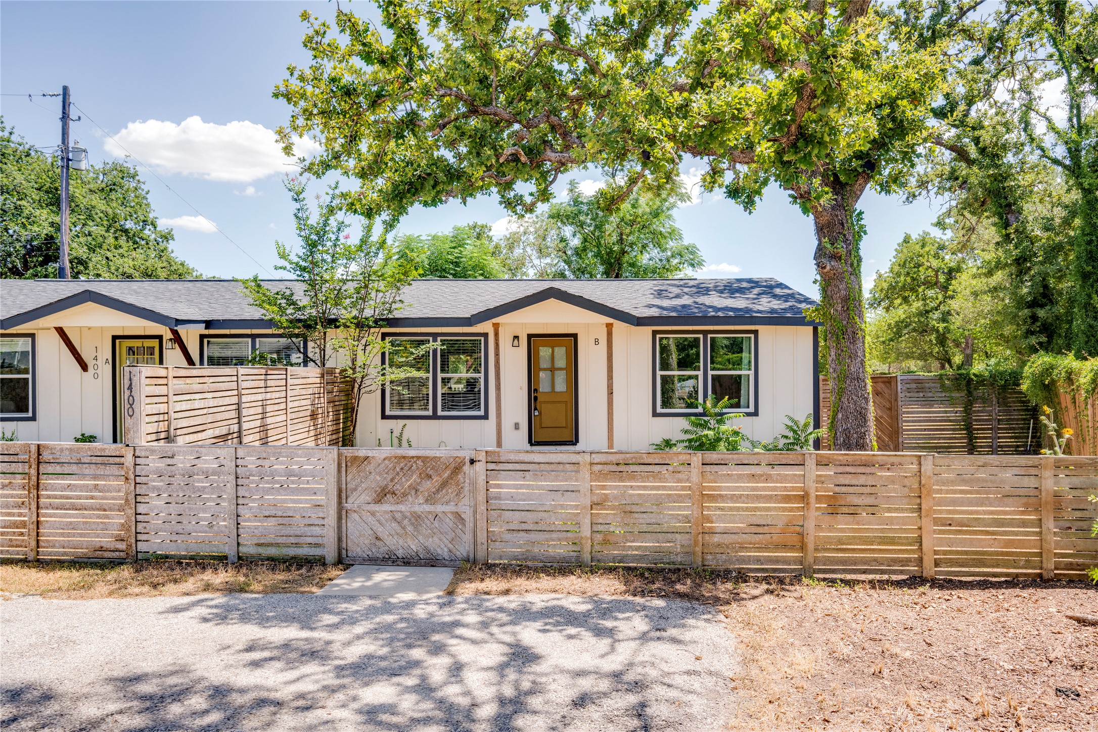 1400 Marcus Place, Unit B Austin, TX 78721 - Photo 4 of 39 A charming single-story residence with modern farmhouse aesthetics, framed by a mature shade tree and a slatted privacy fence.
