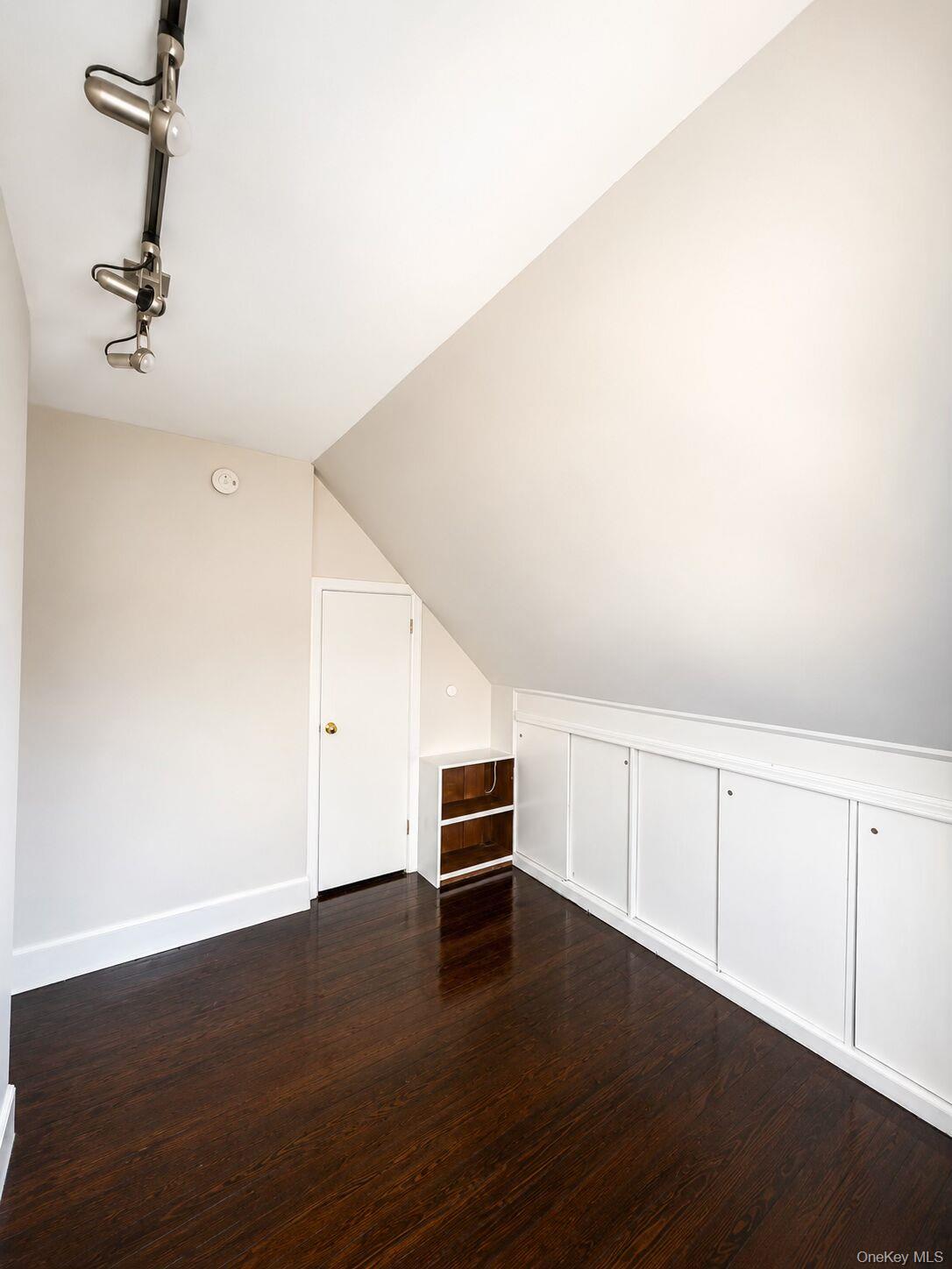 79 Division Street, Unit 3 New Rochelle, NY 10805 - Photo 7 of 17 Second bedroom featuring wood-finish flooring, track lighting, and a white paneled storage unit built into the sloped wall.
