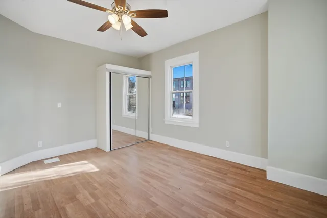 an empty room with wooden floor chandelier fan and windows